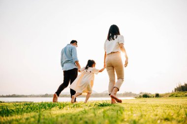 Mutlu bir aile yaz tatilinde eğleniyor ve birlikte oynuyor, doğada koşuyor ve gülüyor, etraflarında güneş ve yeşil çimenler, aile günü