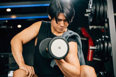 Ağır bir dambıl tutan kaslı bir adam kol kaslarının ve pazılarının gücünü ve sağlıklı bir vücut ve zihin için ağırlık kaldırmanın önemini gösteriyor. boş boşluk