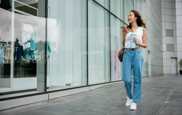 现代生活方式 在繁华的城市街道上散步时 女人拿着一个大杯子 浏览着她的智能手机 — 图库照片