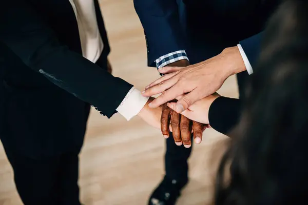 Business professionals gather in a modern office, their hands stacked in a circle as a symbol of achievement and unity. The scene exemplifies cooperation, communication, and a diverse workforce.