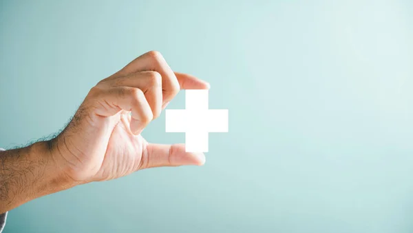 A hand holds a plus icon for medical care, signifying advantages. Health insurance health concept featuring access to welfare health and spacious copy area.