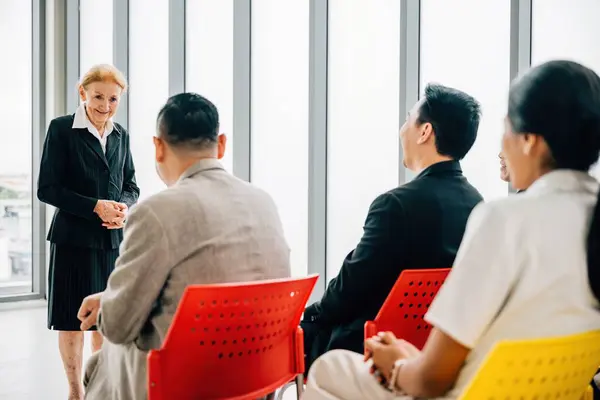In a dynamic office meeting, a confident senior corporate coach delivers a seminar to a business team. The female director, CEO, and employees actively participate, discussing projects and guiding.
