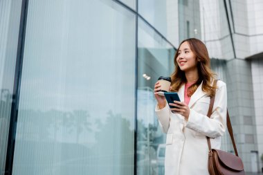 Etkili bir iş kadını, birden fazla işte ustalaşıyor, elinde kahve ve akıllı telefon tutuyor, işe giderken üretken kalıyor..