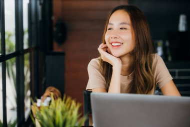 Kafe masasında dizüstü bilgisayarla oturmuş gülümseyen mutlu bir iş kadını. Pencereden dışarı bakıyor. Sabahları kafede gülümseyen güzel bir kadının portresi.