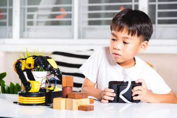 Happy Asian little kid boy using remote control playing robotic machine arm for pick up wood block, Funny child learning successful getting lesson control robot arm, Technology science education