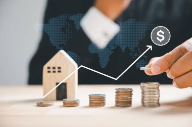 El yığına madeni para ekler, gayrimenkul yatırımını sembolize eder. Ahşap ev, emlak büyümesini ve ipotek finansmanını simgeliyor. Yatırım yoluyla zenginlik inşa etmek gereklidir. Özellik Vergileri