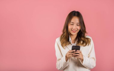 Mutlu bir Asyalı portresi güzel tatlı bir genç kız gülümseyen heyecanlı akıllı cep telefonu stüdyosu pembe arka planda izole edilmiş bir kadın şaşırmış ve akıllı telefondan internetten SMS sohbeti yapıyor.