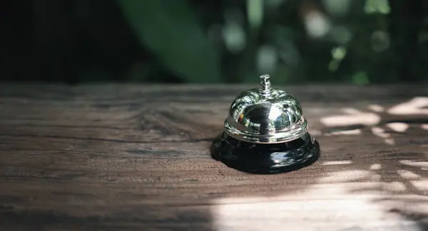 Hotel ring bell. Closeup of silver service restaurant bell on wooden counter desk, vintage bell to call staff outdoor in garden with green leaf