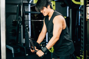 Sporcu, ön ve arka kaslarını çalıştırmak için kablo makinesiyle egzersiz yapıyor, kol ve kollarını kullanarak trisepsi çekiyor. Üst vücut kuvveti egzersizi.