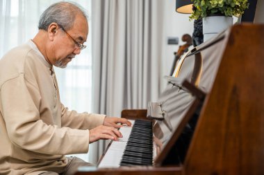 Asyalı emekli adam evde piyano çalmayı öğreniyor yaşlı adam evde piyano çalıyor emeklilikten sonra yaşam tarzı, parmakları klavyede birbirine dokunuyor.