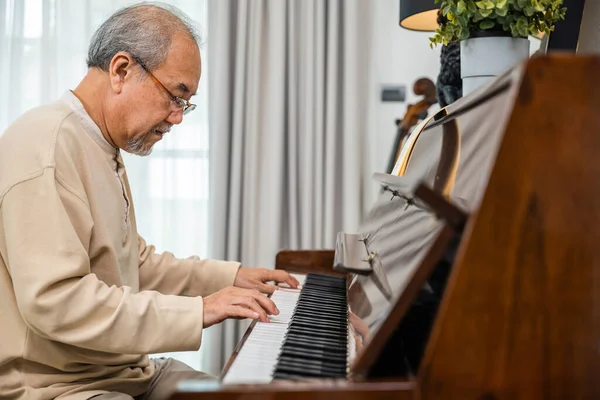 Asian senior retired man learning to play piano at home, Old man playing music on piano in living room at home, lifestyle life after retirement, fingers touching on keyboard