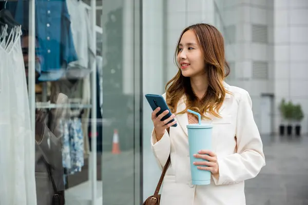 Busy lifestyle in the city ,young woman holding a tumbler mug and smartphone while multitasking. Hot beverage and smart technology in one.