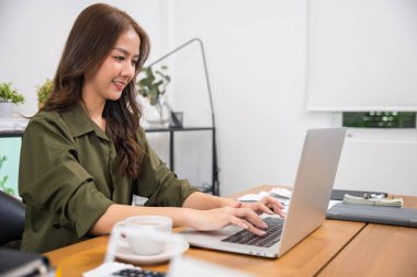 Ofiste dizüstü bilgisayarda çalışan güzel bir kadının portresi, gülümseyen bir iş kadını sabahları dizüstü bilgisayarda klavye kullanarak oturuyor, online alışveriş satışlarını kontrol ediyor.