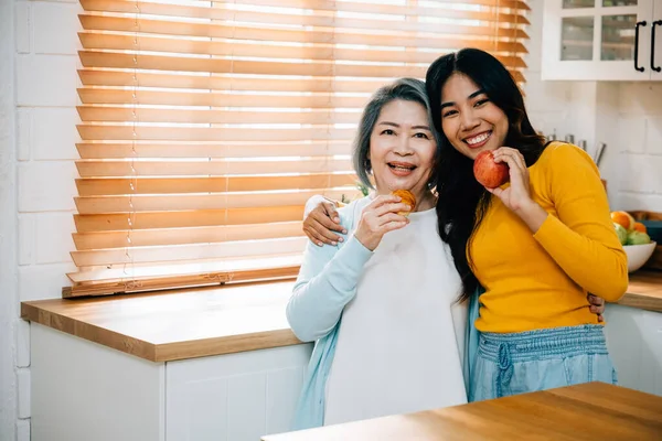 Kitchen scene at home features an elderly mother and her daughter, young Asian woman. moment of togetherness while daughter teaches and assists her mother. beautiful portrait of family bonding.