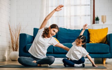 Yürek ısıtan bir aile yogası seansında bir anne ve kızı, beraberliklerini yansıtan gülümsemelerle uyum ve mutluluk bulmaya çalışır..