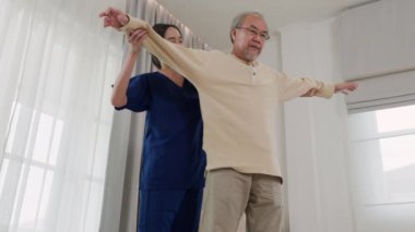 Rehabilitation of disabled people. Old senior man enjoys training with physiotherapist for outstretched arms at home, Asian physical therapist patient help elderly exercising arm stretch