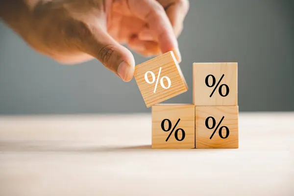 Concept of interest rate and financial rates. Hand placing a wooden cube block on top, symbolizing an increase, with an upward direction icon and percentage symbol.