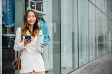 Bağlı ve mutlu, gülümseyen genç bir kadın siyah bir arkaplan önünde bardak ve akıllı telefon tutarken. Dijital iletişim ve mutluluk bir arada..