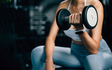 Spor salonunda fitness meraklısı bir antrenman, ağırlık kaldırmak ve vücudunu güçlendirmek ve güzelliğini korumak için dambıllarla egzersiz yapmak.