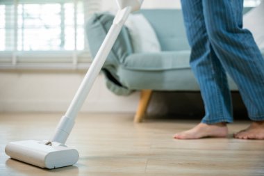 Ev hanımı kadın toz temizleme koltuğun altında ya da koltuk mobilyalarının altında elektrikli süpürgeyle mutlu Asyalı genç kadın evde elektrikli süpürge ile oturma odasında, ev ve ev işi konseptinde.