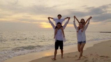 Baba, oğul ve anneyi omuzlarında taşır yaz kumsalında yürürken, ebeveynler gün batımında çocukları sırtında taşır, aile yaz tatilinde, mutlu aile tatilde.