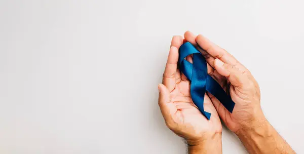 Supporting mens health awareness in November, hands hold a blue ribbon, emphasizing the importance of prostate cancer awareness and support for patients and families.