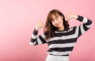 Stüdyoda pembe üzerine çekilmiş Asyalı bir kadın, neşeli bir gülümseme ve olumlu bir jestle anlaşma ve başarı ifade ediyor. Pozitif tavrı bulaşıcı..