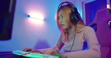 Young player woman wearing gaming headphones intend to do playing live stream games online at home, Happy Gamer endeavor plays online video games tournament with computer desktop with neon lights