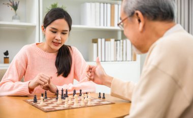 Beautiful young smile woman having fun sitting playing chess game with senior elderly at home, nurse caregiver in nursing home for leisure, Happy active retired people, Healthcare and medical concept