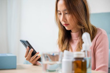 Hasta kadın hapları arıyor ve malzeme etiketini ve ilaç şişesini kontrol ediyor, Asyalı hasta genç kadın akıllı cep telefonuyla ilaç reçetesi okuyor, akıllı telefon online eczane kavramı