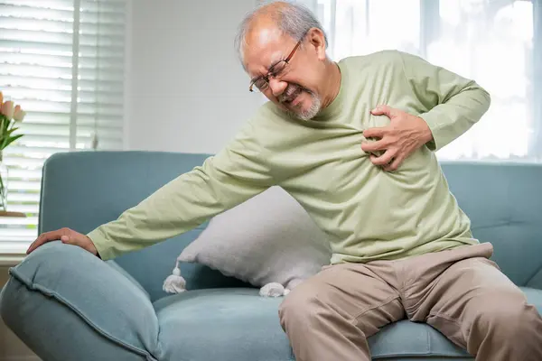 Sad senior man feeling bad pain use hand touching chest having heart attack on sofa in living room, Worried Asian old man have congenital disease suffering from heartache alone at home his heart aches