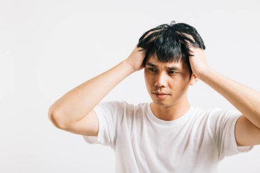 Üzgün ve yorgun yüzlü, stres ve şiddetli baş ağrısı yüzünden başını umutsuzluk içinde tutan Asyalı genç bir adamın portresi. Stüdyo görüntüsü beyaz üzerine izole edilmiş, sıkıntısını simgeliyor..