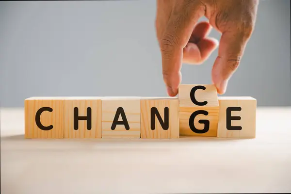 CHANCE emerges as CHANGE flips on wood block in businessman hand. Success, strategy, and positive mindset symbolized. Vintage table enhances visual appeal. Change is evident.