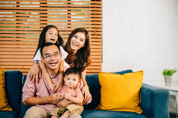In their comfortable modern home an affectionate Asian family dad mom and daughter cuddle on a sofa sharing laughter and bonding during self-isolation. Happiness and togetherness shine through.