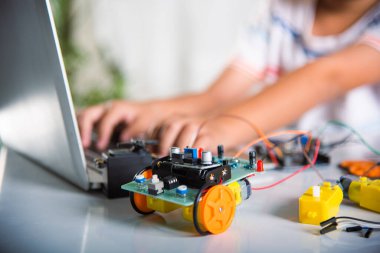Asyalı çocuk, Arduino robot arabası için dizüstü bilgisayarla kodlama ve programlama öğreniyor, küçük çocuk öğrenciler, araba oyuncağıyla bilgisayar kodları yazıyorlar, STEAM eğitim teknolojisi kursu öğreniyor.