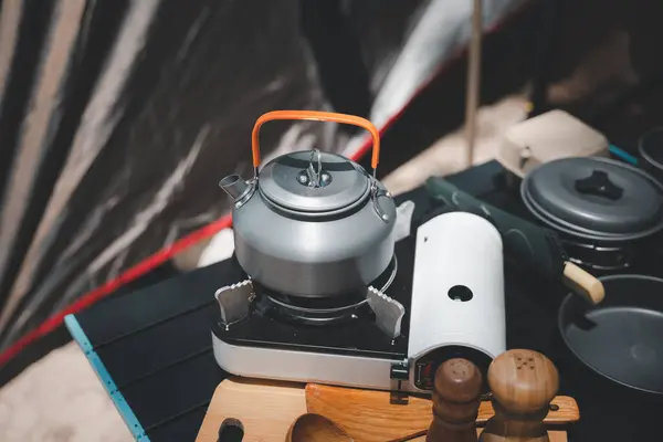 Prepare your campsite feast with this complete set, kettle, pot, pan, gas stove, flashlight, and camera, arranged by the tent at the beach. Camping in style and comfort.