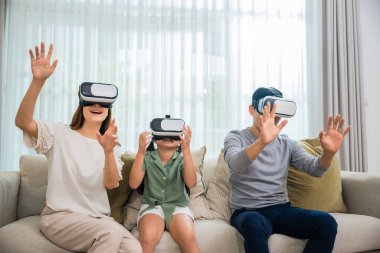 Happy family have mother father and daughter watching movie or playing video game, Asian family wear vr glasses headsets fun sitting on sofa in living room, game entertainment innovation technology