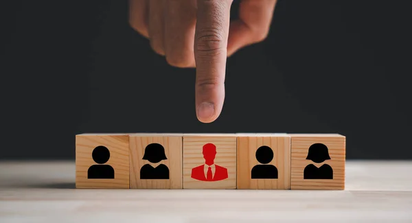 Human hand pointing to a red human icon on a wooden block. Business hiring and recruitment in HR Management. Choose a new leader or new employees to drive business growth. Human resources