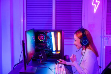 Zafer kazanmak. Asyalı oyuncu çevrimiçi video oyunu oynuyor masaüstü bilgisayarda heyecan verici PC renkli neon ışıklar, oyun kulaklıklı kadın bilgisayar kullanıyor başarılı, E-Sport konsepti, kenar görüş