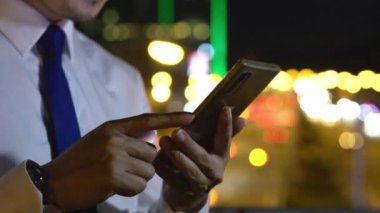 Young man walking and chatting on mobile phone with friends at social networks outdoor, Portrait Asian businessman typing an sms message via smartphone after work near office at night city street