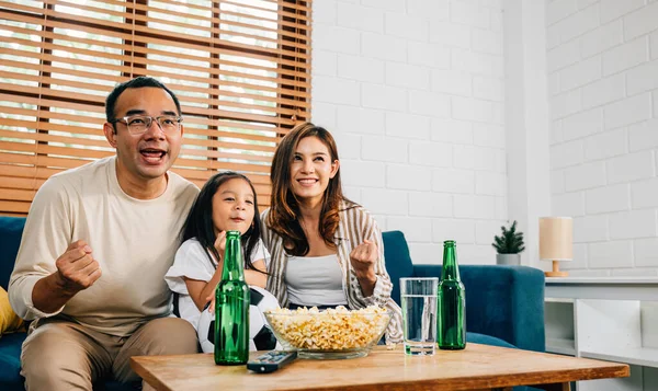 In their cozy living room, a joyful family of fans bond over a football match on TV, celebrating their teams success with cheers and excitement. The room is filled with togetherness and happiness.