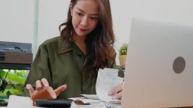 Asian female calculating family budget financial and accounting at home, young woman working with financial data calculator with tablet computer and writing make note calculate, pay bills tax online