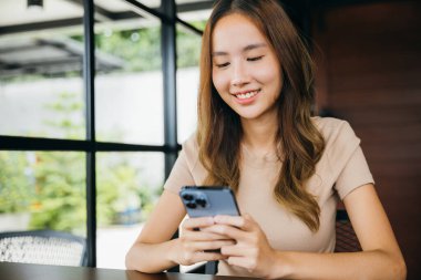 Güzel bir Asyalı kadın havale yapıyor. Finansal internet bankacılığı cep telefonunda. Genç bir kadın sabahları pencerelerin yanındaki kafede online alışveriş yapmak için akıllı telefon kullanıyor.