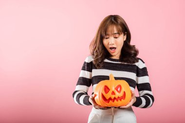 Cadılar Bayramı temalı bir stüdyo çekiminde, Asyalı bir kadın pembe arka planda hayalet şekilli bir balkabağı tutuyor. Onun komik kostümü Cadılar Bayramı atmosferine katkı sağlıyor..