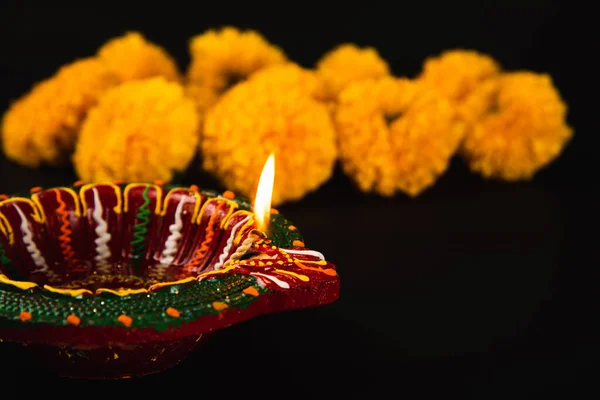 Diwalis beauty revealed, A beautifully adorned Diwali lamp and ornate flower rangoli on a dramatic black backdrop. Ideal for festive invitations, ceremonies, and celebrations.
