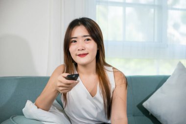 Asyalı genç bir kadın gülümsüyor. Oturma odasında televizyon seyrediyor. Uzaktan kumandalı koltuklar tutuyor.