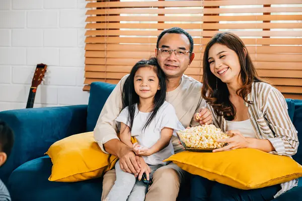 Family bonding with popcorn watching a movie in the living room. The father mother son daughter and schoolgirl enjoy togetherness and happiness during their quality time.