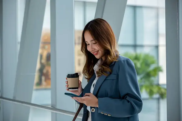 Asian woman holding coffee cup and smartphone on escalator. Perfect for on-the-go and work-related themes. City road background. Business lifestyle on the go concept
