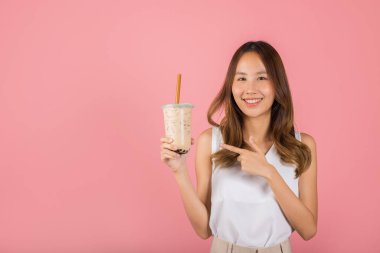İnci sütlü çay içeceği konsepti. Kahverengi şeker aromalı tapyoka içen Asyalı güzel genç kadın sütlü çay ve işaret parmağı, pembe arka planda izole edilmiş gülümseyen kadın portresi.
