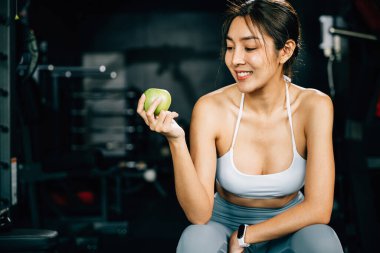 Spor salonunda yeşil elma tutan bir bayan sporcu spor ve egzersiz performansı için uygun beslenmenin önemini vurguluyor. Sağlıklı zindelik ve yeme tarzı konsepti